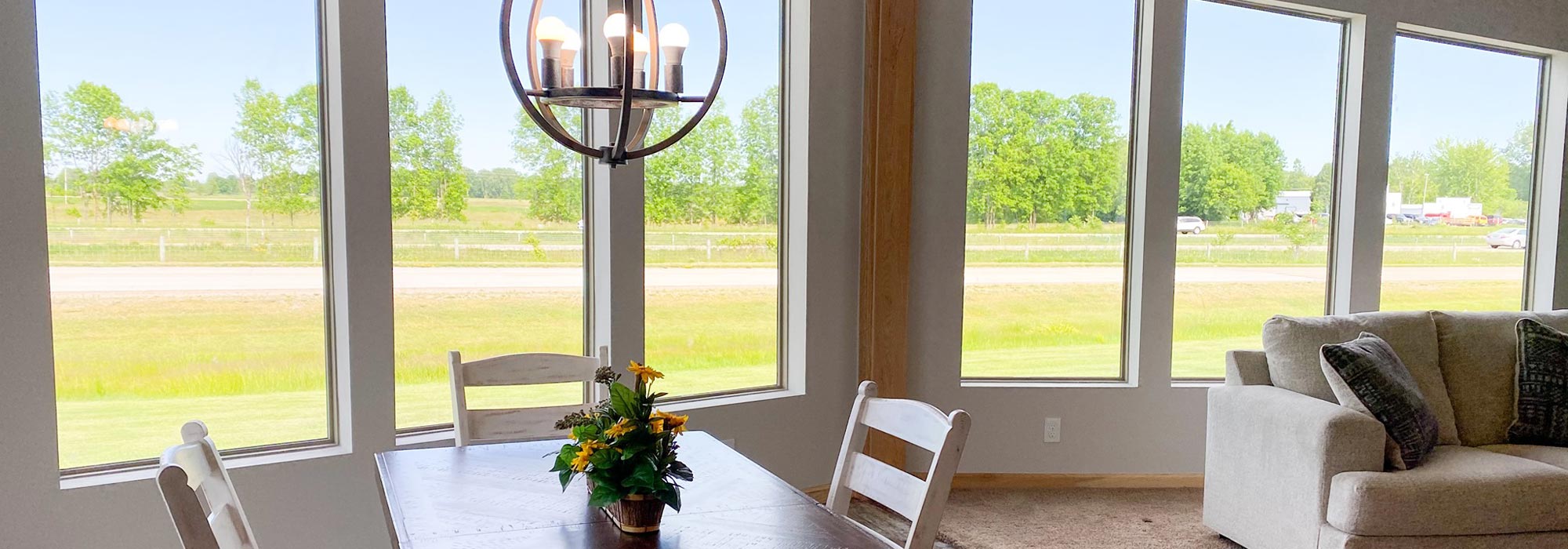 indoor picture of wall of windows in model home with dining room chairs and table, and a couch in the background
